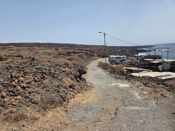 Pista de acceso con coches aparcados junto a pequeñas construcciones pesqueras en la costa del malpaís.