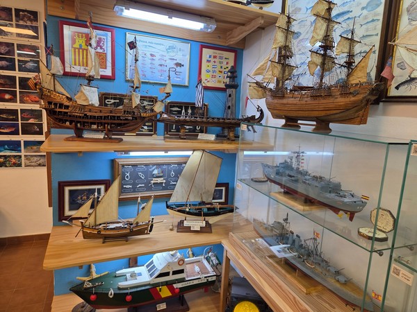Estanterías con maquetas de barcos junto a un timón de madera en el Museo del Pescador.