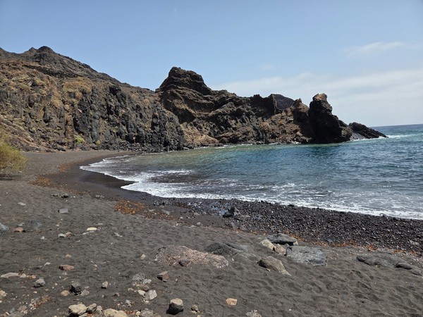 Arena volcánica negra y acantilados basálticos que cierran la bahía de la playa de Roque Bermejo, dentro del Parque Rural de Anaga.