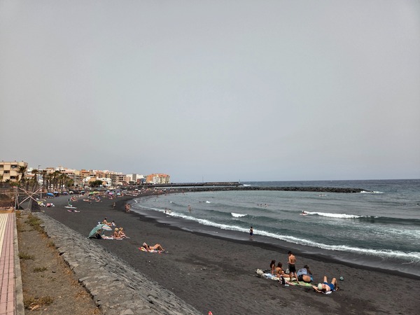 Panorámica de la playa de arena negra del Puertito de Güímar con rompientes suaves y espigones protectores.