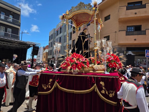 Paso de San Benito Abad decorado con flores rojas y panes, escoltado por romeros en vestimenta tradicional.