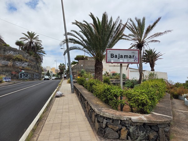 Cartel de entrada con el nombre Bajamar junto a la carretera y palmeras.