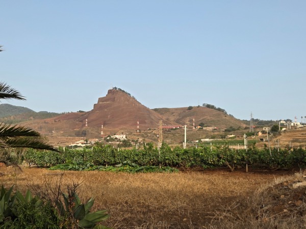 Montaña de tonos rojizos con antenas y viñedos a sus pies en el municipio de El Rosario.