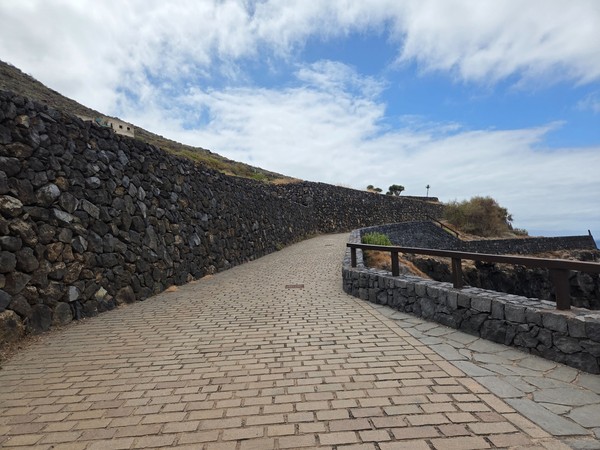 Camino empedrado con muros de piedra volcánica y barandillas de madera.