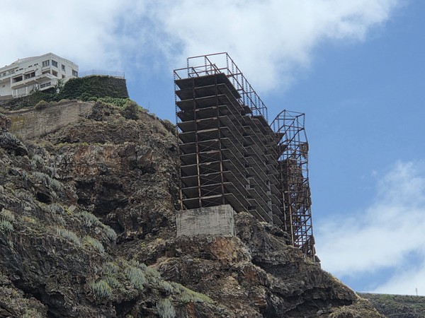 Estructura metálica abandonada adosada al acantilado sobre un gran pedestal de hormigón.