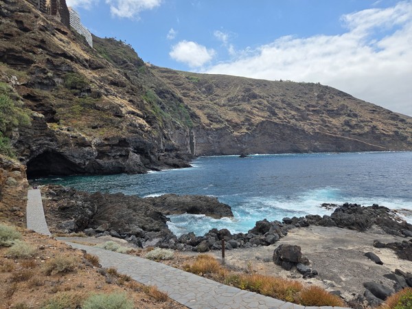 Bahía protegida por paredes rocosas donde el sendero desciende hasta la orilla.