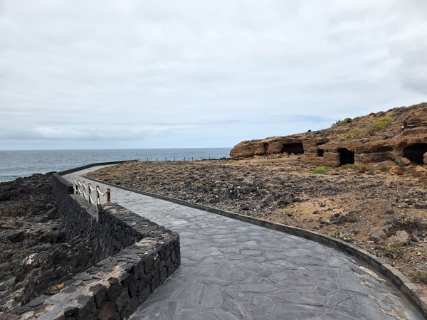 Paseo a ras de costa con barandilla de cuerda y cuevas en la toba volcánica.