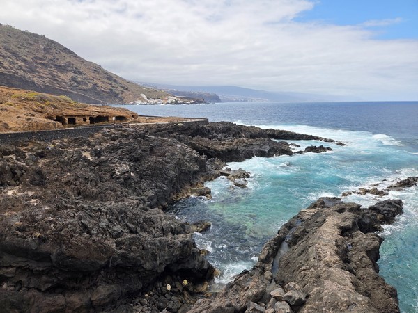 Paseo adoquinado junto a un frente de toba con varias cuevas abiertas al océano.
