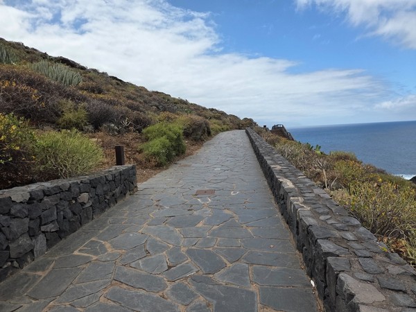 Tramo recto del sendero con muretes de piedra y vistas abiertas al Atlántico.