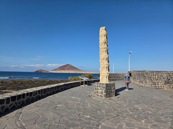 Monolito escultórico junto al mar frente a Montaña Roja en el extremo del paseo de El Médano.