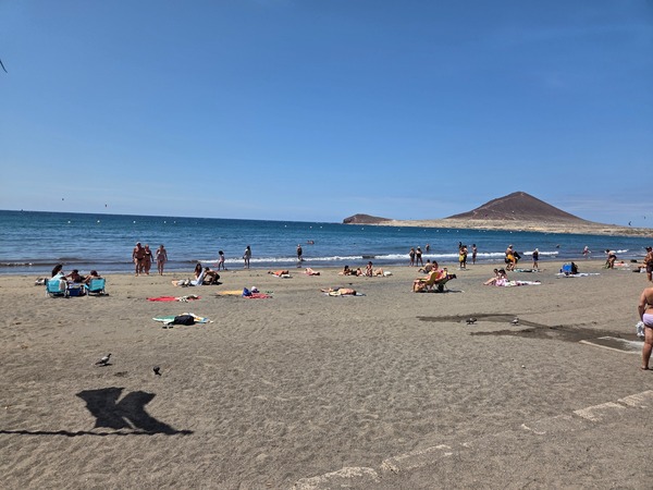 Baños de sol y ambiente familiar en la playa de El Médano con Montaña Roja y cometas de kitesurf a lo lejos.