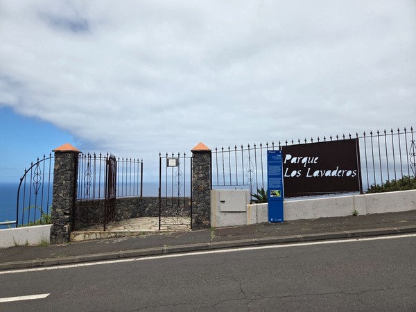 Entrada enrejada y rótulo de Parque Los Lavaderos con el mar asomando detrás.