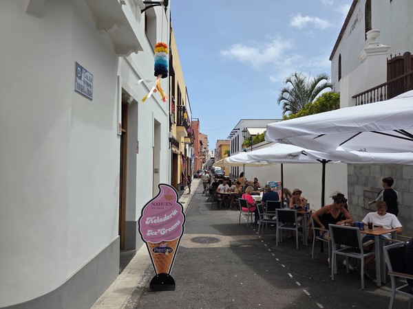 Calle estrecha con terrazas, sombrillas blancas y gente disfrutando en el centro de Garachico.