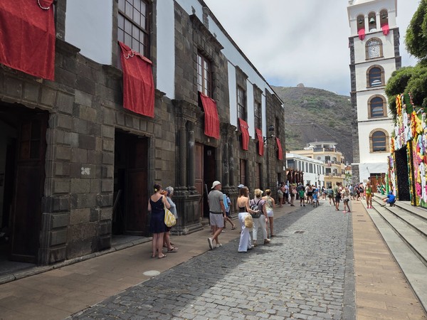 Calle empedrada con casas históricas, paños rojos en balcones y torre campanario en Garachico.
