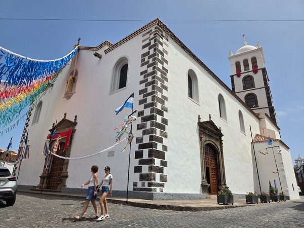Vista oblicua de la Iglesia de Santa Ana con torre, portadas de piedra y banderolas festivas.