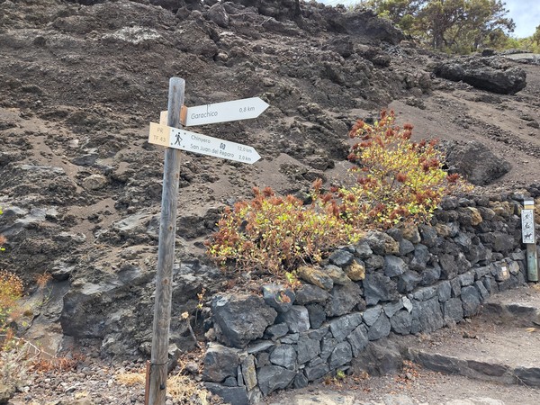Poste de senderismo que indica Garachico, San Juan del Reparo y Chinyero sobre terreno volcánico.
