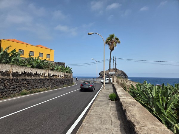 Carretera de acceso a Garachico con muros de piedra, plataneras y el Roque al fondo junto al océano.
