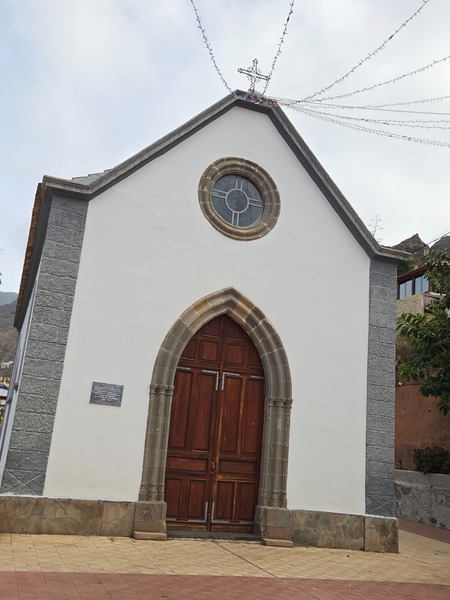 Ermita blanca con portada de cantería volcánica y puerta de madera.