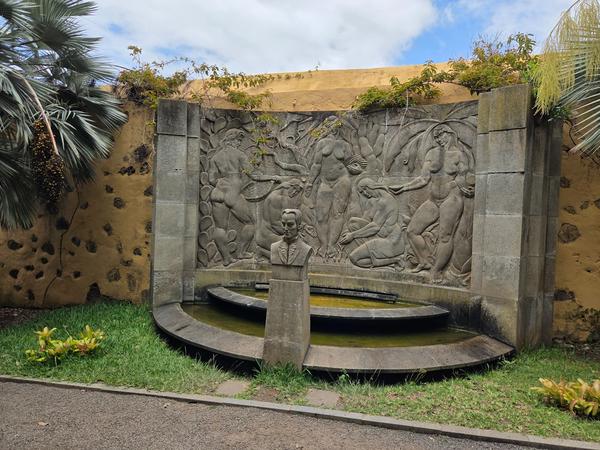 Escultura de busto frente a mural tallado con figuras humanas