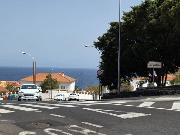 Cartel de acceso que indica el barrio de Las Caletillas con el mar al fondo.