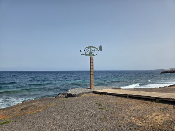 Escultura del pez junto al litoral rocoso de Las Caletillas con el océano Atlántico.