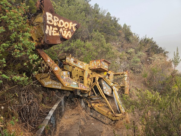 Retroexcavadora amarilla oxidada y cubierta de pegatinas junto al canal en la ladera.