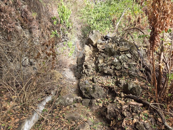 Derrumbe de rocas y tierra que obstruye parcialmente el sendero junto al canal.