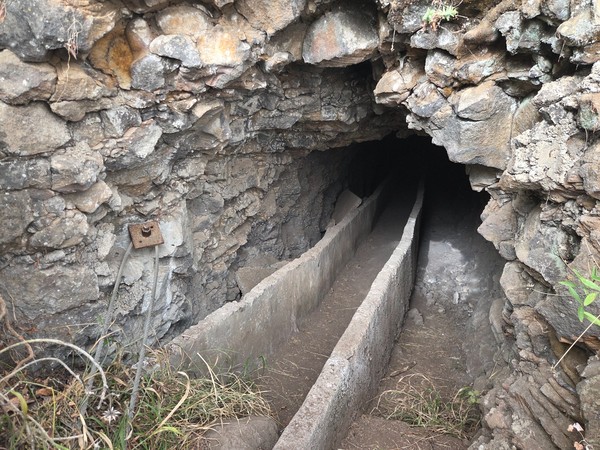 Entrada de la galería con canal de agua excavado en la roca y acceso estrecho.