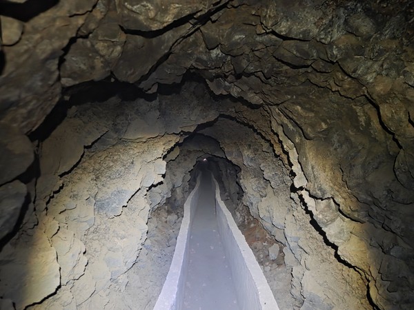 Interior de la galería de agua con canaleta central y paredes volcánicas, iluminado con frontal.