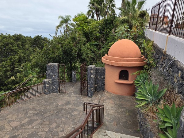 Acceso con cúpula de color terracota y escalones que descienden entre muros volcánicos.