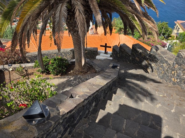 Escalinata amplia con barandillas de piedra y una cruz junto a una palmera.