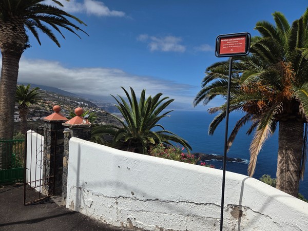 Otra puerta de acceso al recinto de Parque Los Lavaderos con palmeras y el mar al fondo.