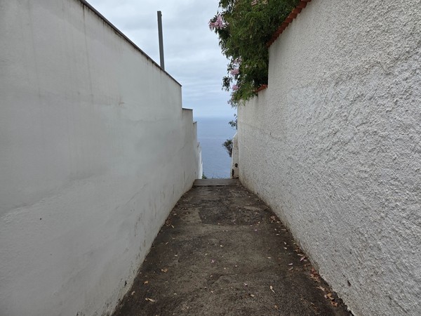 Pasillo de acceso entre muros encalados que conduce hacia el borde del acantilado del Mirador de los 500 Escalones con el mar al fondo.