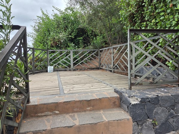 Tramo intermedio de la escalera con barandillas en aspa, muros ocres y suelo de laja volcánica.