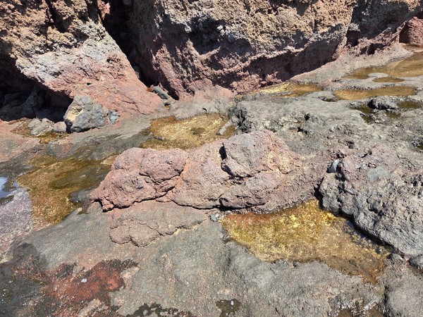 Perfil rocoso en la línea de costa con diferentes capas de lava de color rojizo y gris.