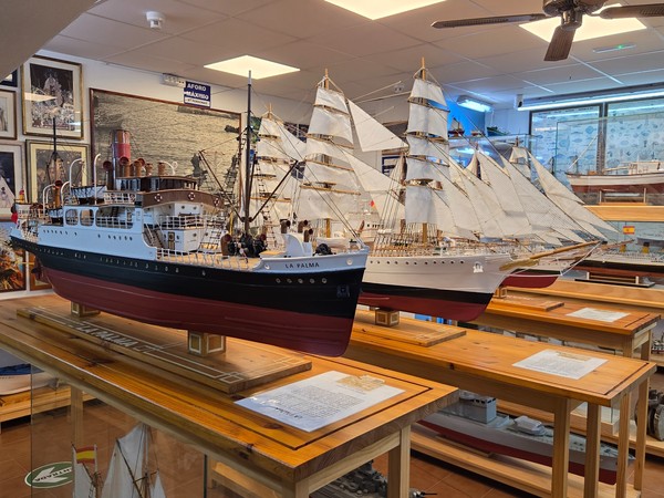 Maqueta de barco frente a un mural con imágenes religiosas y escenas marineras.