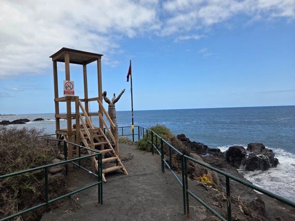 Torre de vigilancia de madera con bandera roja frente al mar en Playa Bollullo