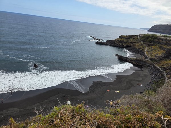 Vista panorámica de Playa Bollullo desde el acantilado, mostrando su arena volcánica negra y el Atlántico