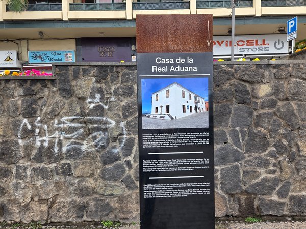 Panel informativo sobre la historia de la Casa de la Real Aduana en varios idiomas.