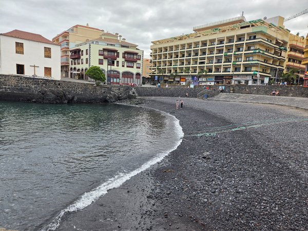 Vista lateral de la playa de callaos y los edificios que rodean la cala del Muelle en Puerto de la Cruz.