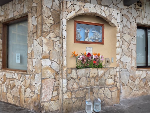 Hornacina con imagen marinera decorada con flores frescas en una fachada de piedra.