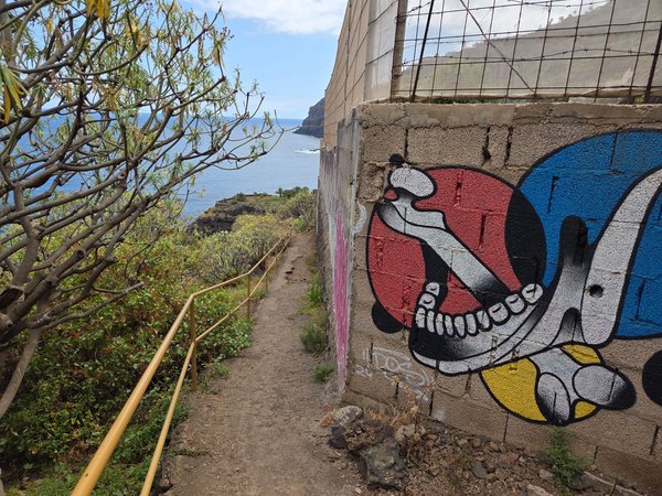 Sendero con barandilla y mural de grafiti que desciende hacia la costa, ofreciendo vistas al océano desde El Ancón.