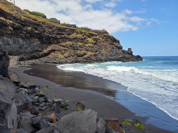 Panorámica de Playa El Ancón con acantilados volcánicos y espuma blanca del Atlántico bajo un cielo despejado.