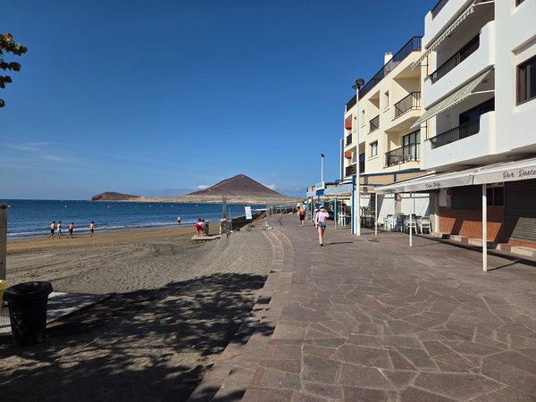 Paseo marítimo de El Médano con cafeterías y vistas a la playa de arena volcánica.