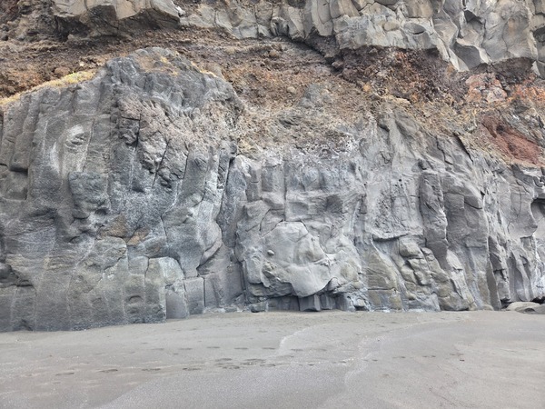 Arco natural de lava erosionado por el oleaje bajo una pared de columnas basálticas en la Garañona.