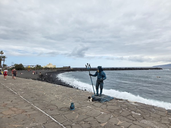 Artista callejero caracterizado como tritón frente al mar en Playa Martiánez.