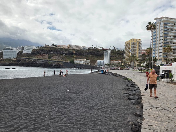 Arena volcánica negra y paseo marítimo con acantilados y hoteles al fondo en Playa Martiánez.