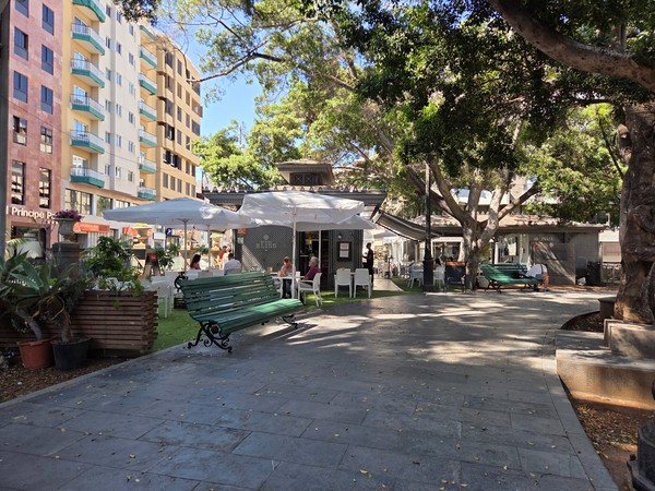 Fachada del kiosco Café Bliss con terraza y bancos verdes en la Plaza Príncipe de Asturias.