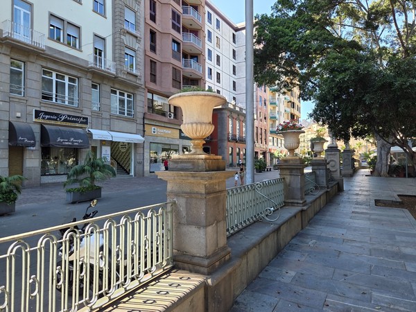 Fachadas comerciales y barandillas de piedra en el perímetro de la plaza, zona peatonal.