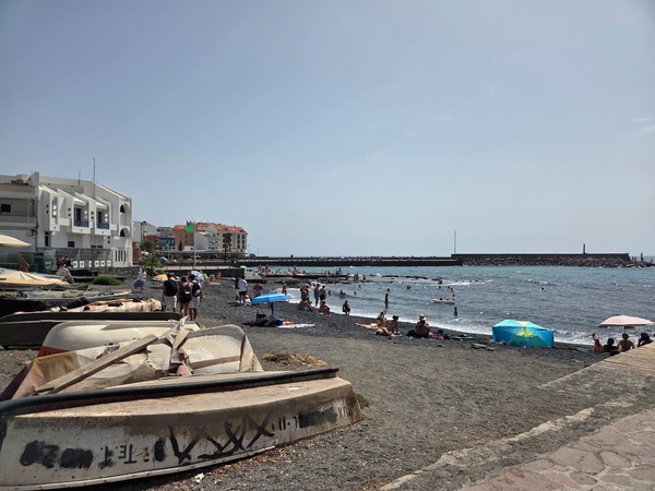 Barcas varadas sobre la arena oscura junto a la playa urbana.